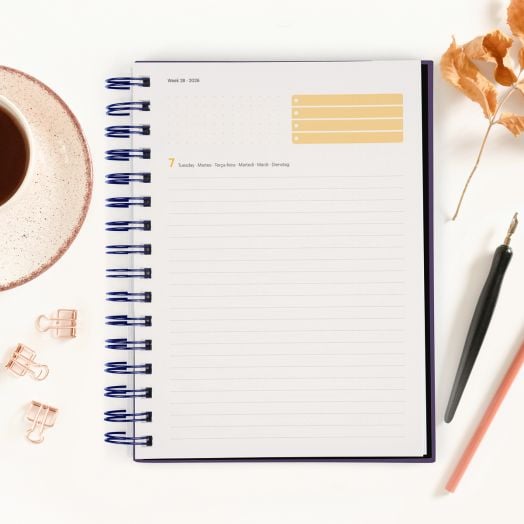 Тефтерът - органайзер Miquelrius Marf Organic Dualidad Floral 2026, ден на страница, е отворен на датирана, подредена страница с жълта зона за проверка, освен кафе, изсушени листа, химикалка и щипки за папки.-3