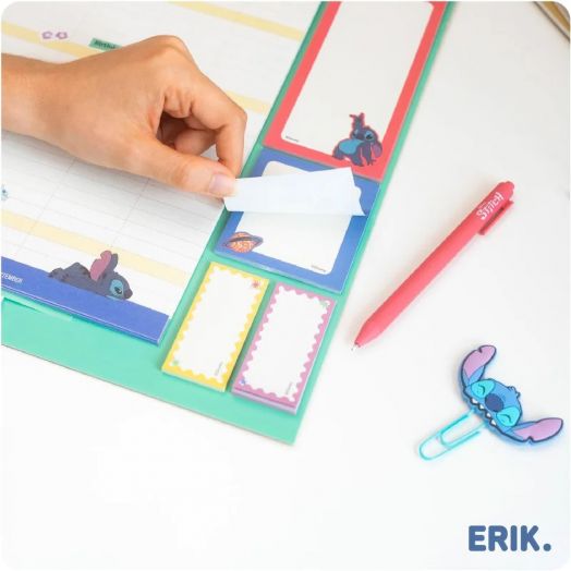 Ръка отлепва лепяща се бележка от 16-месечния блок за планиране Grupo Erik Stitch (септември 2025 г. - декември 2026 г.) с изображение на Stitch, червена химикалка и кламер във формата на Stitch; логото на ERIK се появява долу вдясно.-2