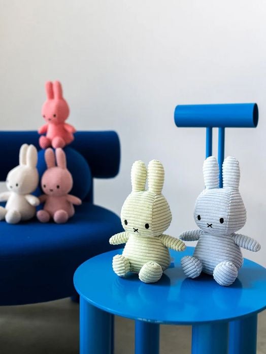 Петима плюшена играчка Miffy Eco Corduroy - светлосин заек, 23 см са разположени върху сини мебели; двама седят на малка синя масичка отпред, трима почиват на съвпадащ диван - очарователен подарък за момченце.-4