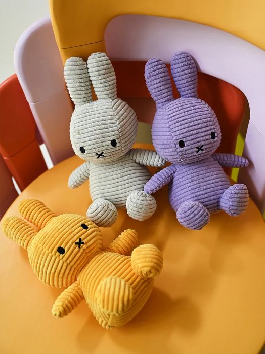 Плюшената играчка Miffy Eco Corduroy с размер 33 cm представлява жълто зайче с черни зашити очи и нос, разположено на оранжев стол с розово-жълта облегалка.-5