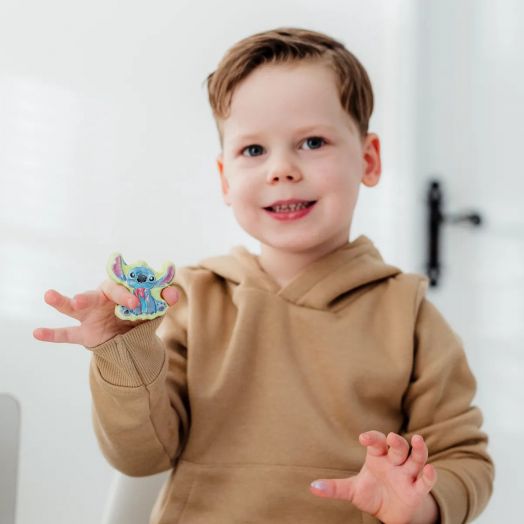 Младо момче в загоряла качулка се усмихва и държи малка синя фигурка от Творчески комплект Totum Stitch - Направи и оцвети гипсови фигури, застанала на закрито на бял фон.-5