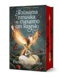 Фантастична книга със заглавие Пойната птичка и сърцето от камък, твърда корица, от Кариса Броудбент представя светеща птица на клон с червени плодове на мистичен фон. Страниците с червени кантове и дизайнът на златна стрелка придават стил на очарователно
