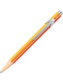 Шестоъгълна Химикалка Caran d'Ache 849 с жълти, оранжеви и червени ивици, метален клипс и бутон в горната част е разположена под ъгъл върху бял фон идеален избор от книжарница Orange за висококачествени продукти.