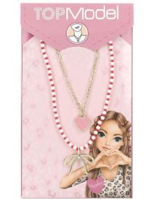 Комплектът Двойно колие Top Mode включва колие от мъниста със златна висулка във формата на панделка и златна верижка с висулка с розово сърце, всички в розова опаковка TOPModel с илюстрирано момиче, което оформя сърце с ръце.