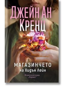 Човек държи с двете си ръце светещ кристал. Корицата на "Магазинчето на Хидън Лейн" е с удебелен розово-бял текст на кирилица, името на автора Джейн Ан Кренц и намеци за паранормални таланти и семейни тайни.
