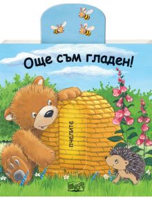 Симпатичен гладно мече седи до голям жълт кошер, протягайки ръка за мед, докато таралеж стои на зелена трева с цветя, а две пчели летят над него. Детската книжка "Още съм гладен" е на български език, със синьо небе и облаци.