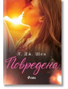 Повредена – Л. Дж. Шен (мека корица, част от поредицата Красиво безразсъдство). Корица на книга с близък план на двойка, която се целува, окъпана в топла, златиста слънчева светлина. Заглавието "Повредена" от Л. Дж. Шен се появява на кирилица в долната ча