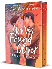 Корица на книгата You've Found Oliver, романтична книга за възрастни, с двама млади мъже, които се държат за ръце сред есенни листа, в топли оранжеви и розови тонове и ръкописен текст на заглавието.